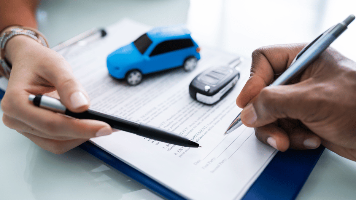 Imagem de duas pessoas (apenas mostrando a mão segurando uma centa) à mesa assinando um contrato. Ao lado há a chave de um carro e um carro em miniatura.