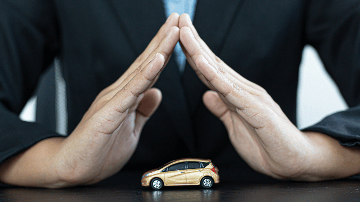 Imagem de um homem (sem mostrar o rosto, apenas as mãos e parte de cima do tronco) protegendo uma miniatura de carro em cima da mesa.