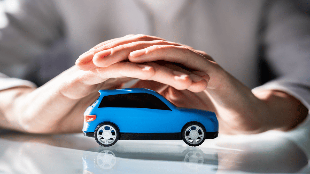 Imagem de uma miniatura de carro e uma pessoa com as duas mãos sobre o carro como se fosse cobrindo a miniatura.